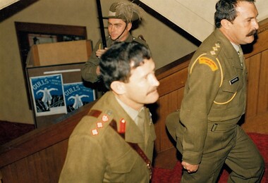 Two officers ascending stairs at theatre with solder wearing hat behind them