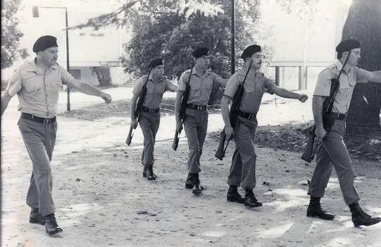 Fiver soldiers marching, trees in background.