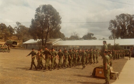 Soldiers marching past an officer on dais.