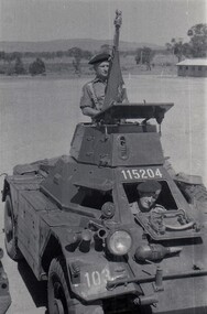 Two soldiers in scout car, one with flag.