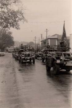 Army vehicles in street on rainy day.