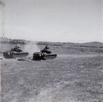 Tanks in paddock firing guns.