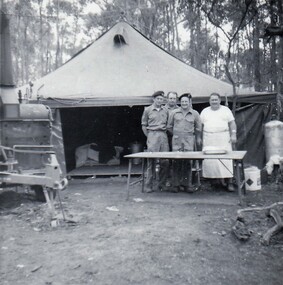 Four soldiers standing behind table in front of tent
