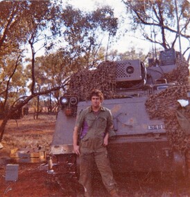 Soldier in uniform standing beside large armoured car.