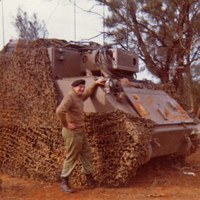Soldier standing beside large armoured car in bushland.