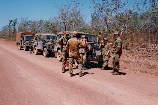 Soldiers and vehicles beside dirt road in bushland.