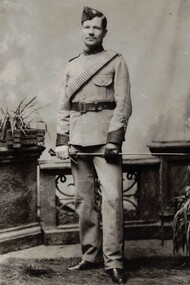 Soldier wearing side cap and holding riding crop.