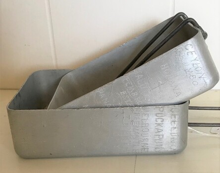 Rectangular metal tins with folding wire handles. One fits inside the other.