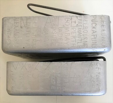 Two rectangular metal containers with handles. The sides of the containers are hand engraved with names of places. 