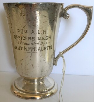 A silver drinking cup with handle and engraving on side.