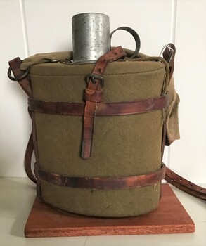 metal container wrapped in felt and held in leather straps, small metal cup in top.