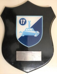 A wooden shield with coloured plaque in the centre and a presentation label.