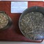 Two tins with plastic lids filled with grain and chaff and attached to a board