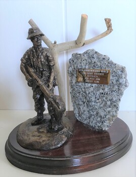 Statue of soldier holding rifle standing beside dead tree and rock.