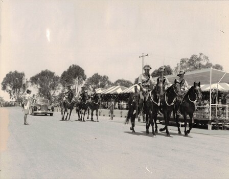 Group of light horsemen followed by large black car.
