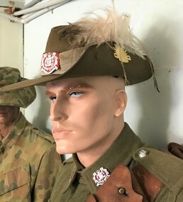 Portrait of mannequin wearing hat with plumes on side of brim.