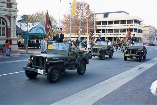 Three jeeps in city centre, men carrying flags.