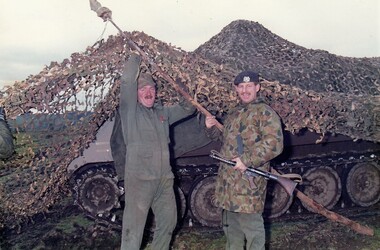 Two soldiers lifting up a camouflage net over tank