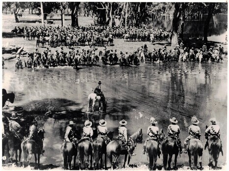 Large gathering of soldiers on horses at waterhole.
