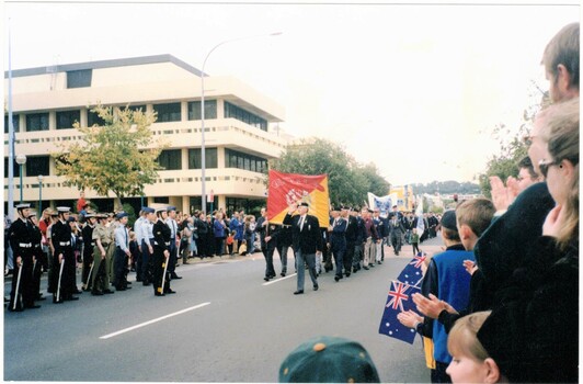 Marching men saluting uniformed guard in street. 