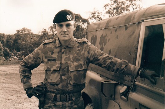 Army officer wearing beret standing beside landrover.