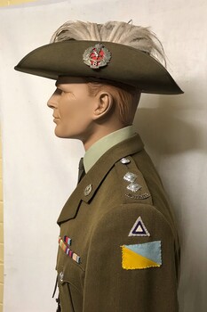 Mannequin wearing hat with badge and plumes.