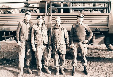 Four soldiers standing beside truck