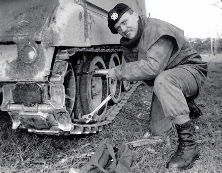 Soldier kneeling beside vehiicle with tracks