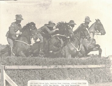 Four horses ridden by soldiers jumping fence.