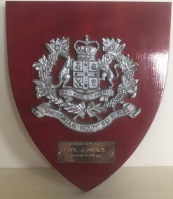 Wooden shield- shaped plaque with silver badge.