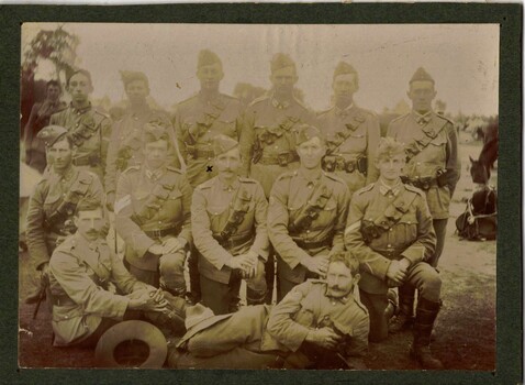 Thirteen soldiers posed in three rows, horse behind.