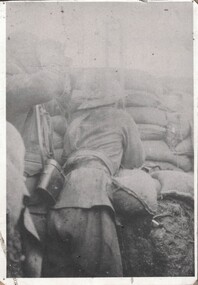 Faded photograph of soldier leaning om sandbag wall