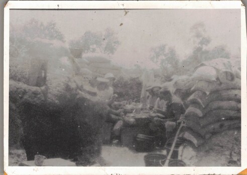 Soldiers sitting round makeshift table in trench.