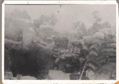 Soldiers sitting round makeshift table in trench.