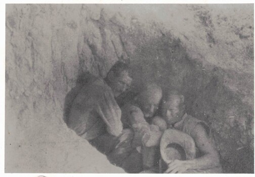 Three men crouched in a dusty hole
