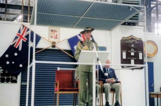 Army officer at microphone on dais.