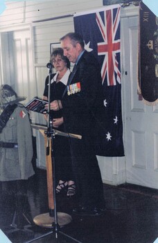 Former serviceman and lady standing in front of flag