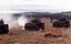 Tanks firing guns on hillside. 