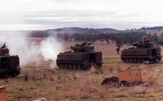 Tanks firing guns on hillside. 