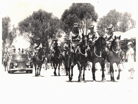 Group of horsemen leading a car.