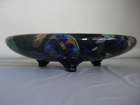 Smooth and glossy ceramic oval shaped shallow bowl with three legs. Dark blue base colour with floral design in blue, purple, yellow and green.