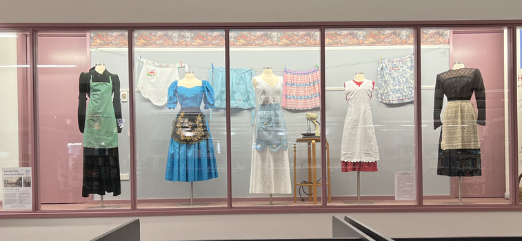 Display of nine aprons and pinafores at Kew Library in 2024