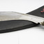 Brass handled, silver blade machette, unsheathed propped across the top of  leather scabbard. On white background