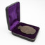 Bronze medallion with depiction of Simpson and his donkey, 1915. In purple, fabric-lined hinged box, opened. Object on white background