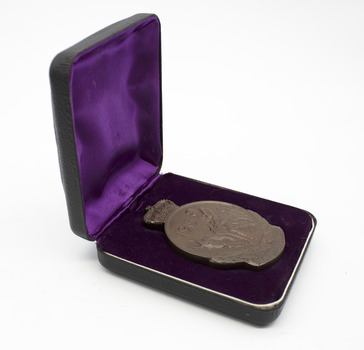 Bronze medallion with depiction of Simpson and his donkey, 1915. In purple, fabric-lined hinged box, opened. Object on white background