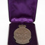 Bronze medallion with depiction of Simpson and his donkey, 1915. In purple, fabric-lined hinged box, opened. Object on white background