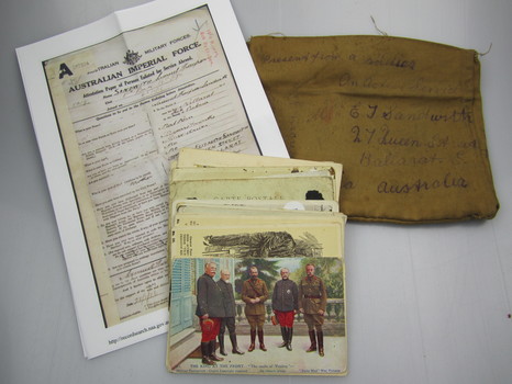 Pile of postcards on top of white paper document printed with black ink on left (appears to be a 'record of service' photocopy) and cloth 'envelope' on right, with address handwritten in ink