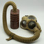Khaki coloured mask with large glass eye pieces and metal respirator at nose, same fabric covered tube from base of mask to top of tin canister. Canister is red/brown colour oval shape, on white background.
