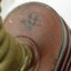 Top of red/brown tin cannister showing detail of inscription and cylindrical hose connected to the the top.