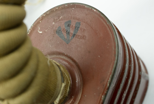 Top of red/brown tin cannister showing detail of inscription and cylindrical hose connected to the the top.